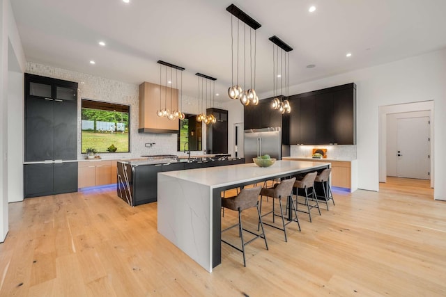 kitchen featuring backsplash, a large island with sink, stainless steel built in fridge, and light wood-style flooring