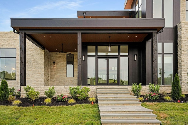 doorway to property featuring french doors, a ceiling fan, a balcony, and stone siding