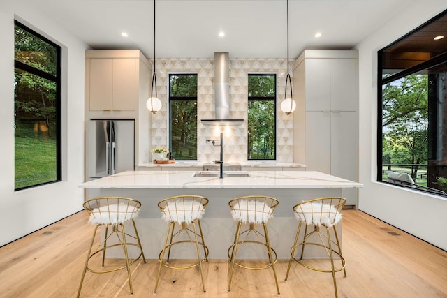 kitchen featuring a sink, a breakfast bar area, wall chimney range hood, plenty of natural light, and high end refrigerator