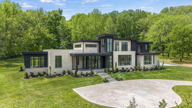 view of front of house with a balcony, a view of trees, a front yard, and stone siding