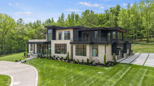back of house featuring a garage, a yard, a balcony, and stone siding