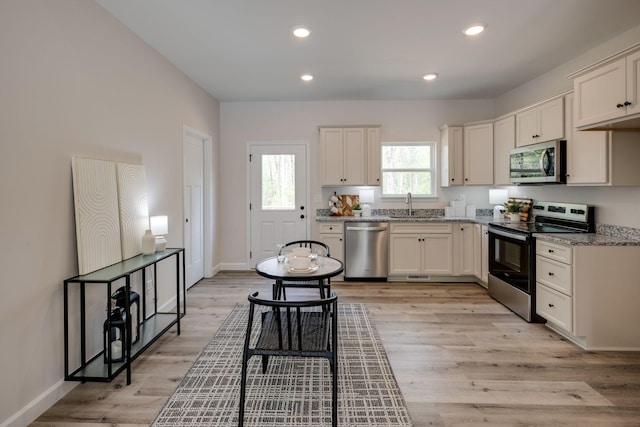 kitchen featuring light stone counters, a sink, baseboards, and stainless steel appliances
