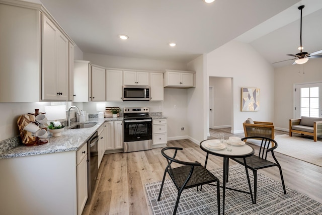 kitchen with a ceiling fan, appliances with stainless steel finishes, a sink, light stone counters, and light wood-style flooring