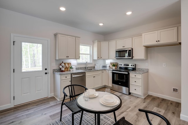 kitchen with stainless steel appliances, light stone countertops, baseboards, and light wood-type flooring