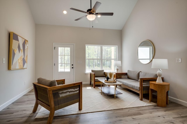 living room featuring ceiling fan, baseboards, high vaulted ceiling, and wood finished floors