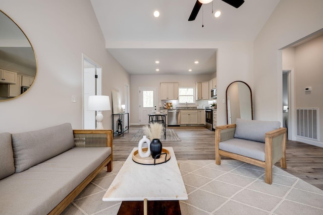 living room with a ceiling fan, visible vents, vaulted ceiling, and light wood-type flooring