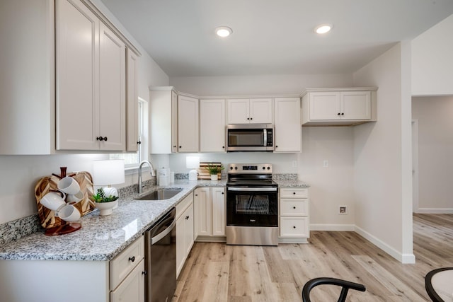 kitchen with light wood-type flooring, white cabinets, light stone counters, a sink, and appliances with stainless steel finishes