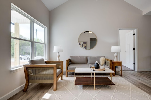 living area with baseboards, light wood finished floors, and high vaulted ceiling