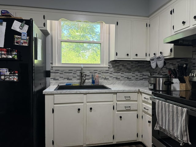 kitchen featuring freestanding refrigerator, electric stove, under cabinet range hood, white cabinets, and a sink