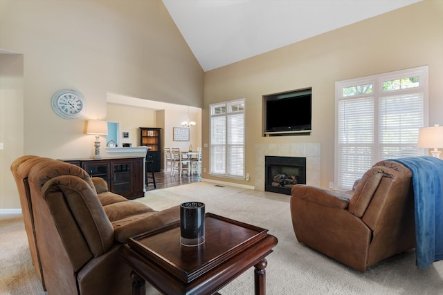 living room featuring a tiled fireplace, high vaulted ceiling, a chandelier, and light colored carpet