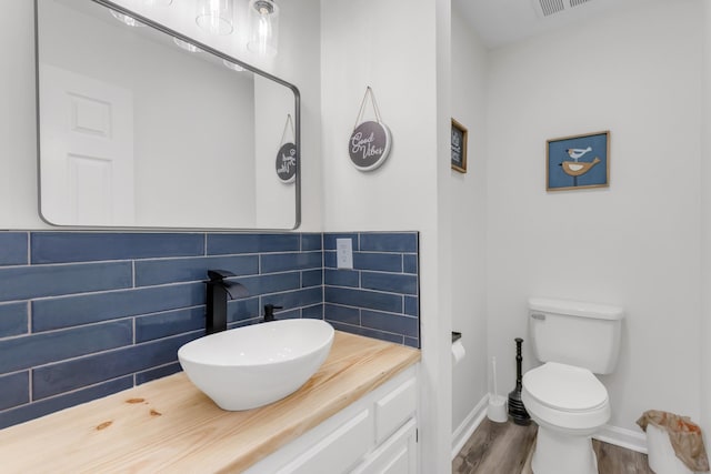 bathroom featuring decorative backsplash, wood finished floors, baseboards, vanity, and toilet