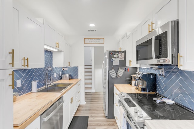 kitchen with a sink, appliances with stainless steel finishes, butcher block counters, and white cabinetry