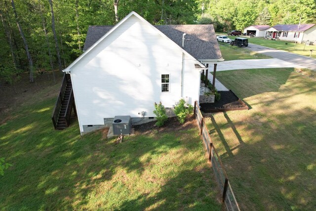 view of side of home featuring crawl space, roof with shingles, a lawn, a wooded view, and stairs