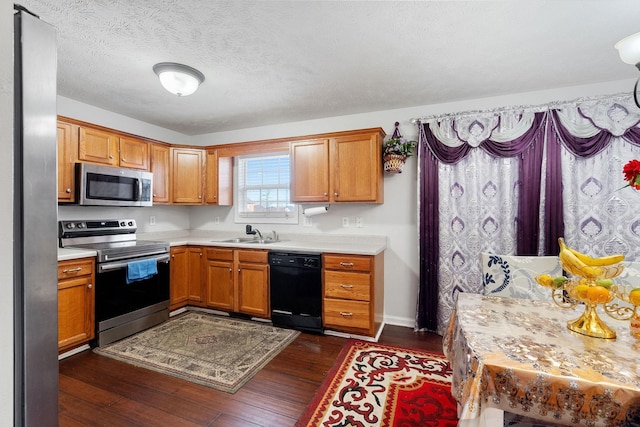 kitchen featuring brown cabinets, dark wood-style flooring, a sink, light countertops, and stainless steel appliances