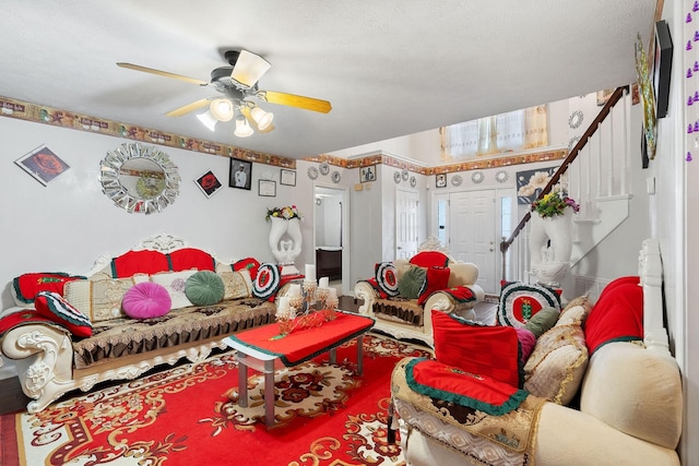 living area with a ceiling fan and stairway