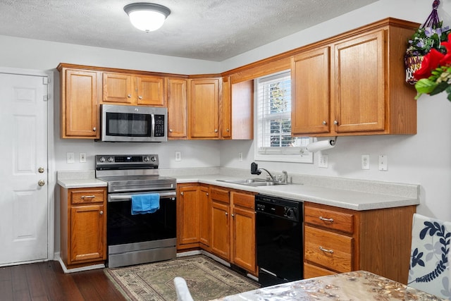 kitchen with brown cabinetry, dark wood-style flooring, light countertops, a sink, and appliances with stainless steel finishes