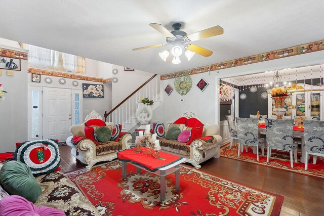 living room with stairway, ceiling fan with notable chandelier, and wood finished floors