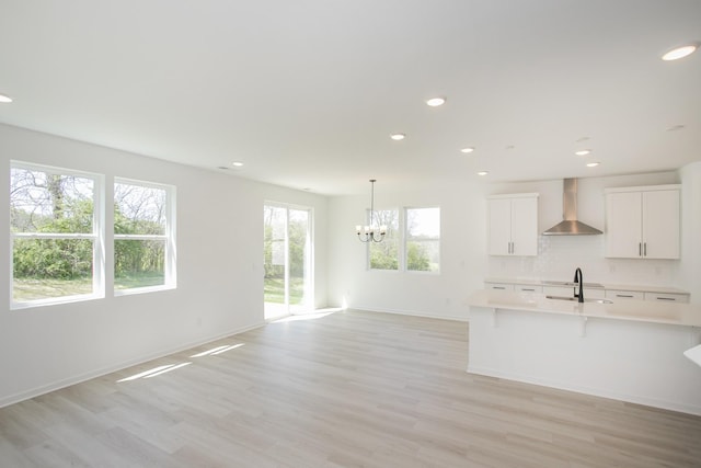 kitchen featuring a sink, light countertops, a chandelier, light wood-style floors, and wall chimney exhaust hood