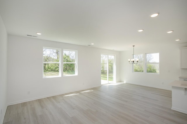 unfurnished living room with an inviting chandelier, light wood finished floors, recessed lighting, baseboards, and visible vents