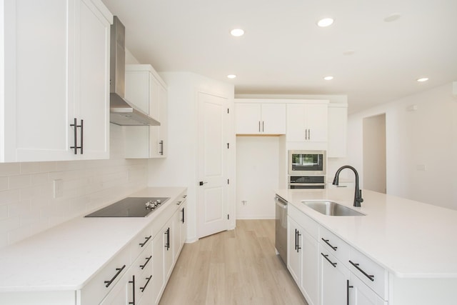 kitchen with tasteful backsplash, light wood-type flooring, a sink, stainless steel appliances, and wall chimney exhaust hood
