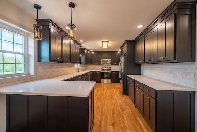 kitchen with decorative backsplash, appliances with stainless steel finishes, light wood-type flooring, a sink, and a peninsula