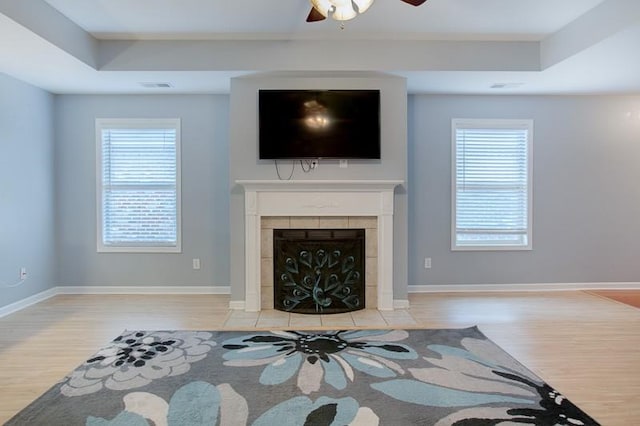 living area featuring ceiling fan, a raised ceiling, wood finished floors, a tile fireplace, and visible vents