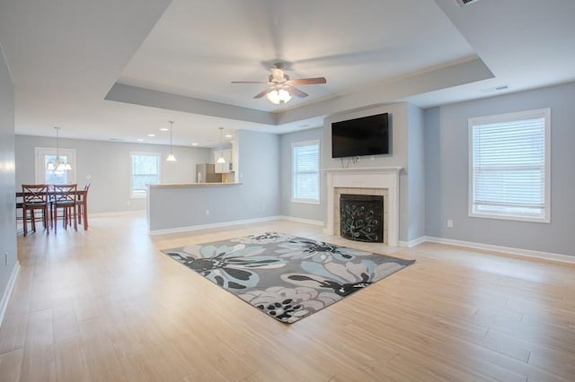 living room with light wood-style floors, a raised ceiling, ceiling fan, and baseboards