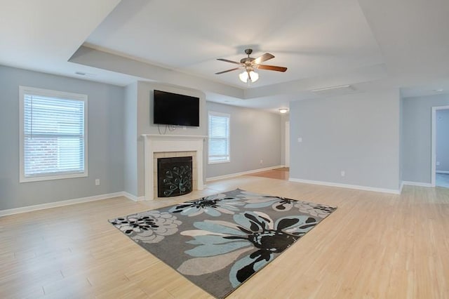 living area featuring a ceiling fan, a fireplace, a raised ceiling, baseboards, and light wood-style flooring
