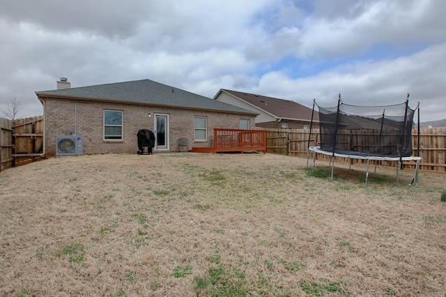 back of house with a deck, a fenced backyard, brick siding, a trampoline, and a yard