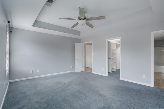 unfurnished bedroom featuring a tray ceiling, visible vents, baseboards, and a spacious closet