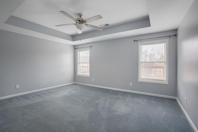 carpeted spare room featuring visible vents, a ceiling fan, baseboards, and a tray ceiling