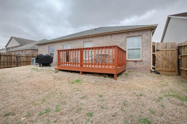rear view of house with brick siding, a fenced backyard, a deck, and a shingled roof