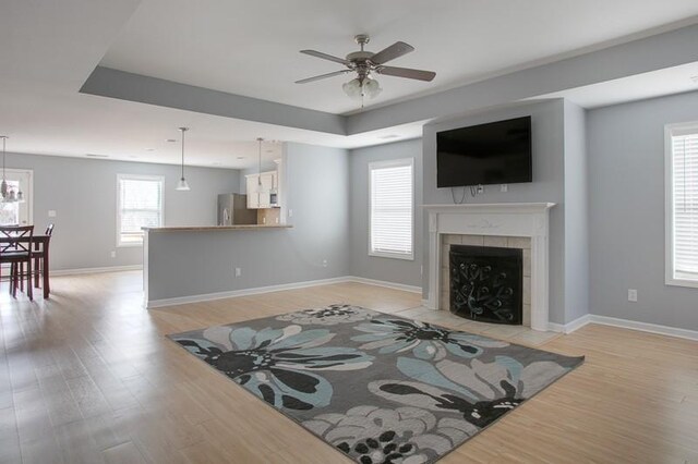 living area featuring a tray ceiling, a ceiling fan, light wood-style flooring, and a tile fireplace