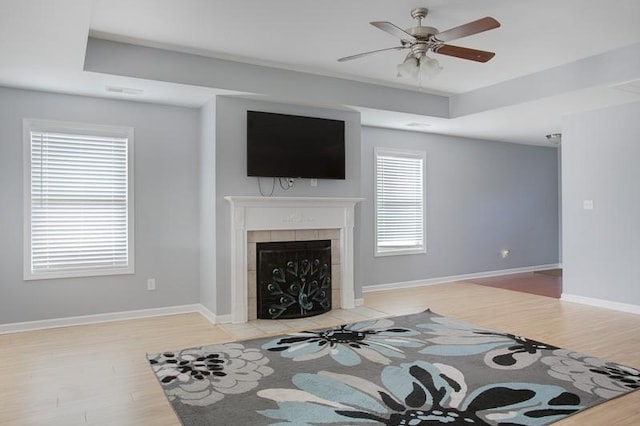 living area featuring ceiling fan, a raised ceiling, light wood-style floors, baseboards, and a tile fireplace