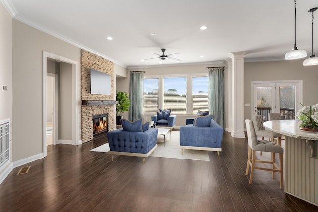 living room with crown molding, ceiling fan, dark wood finished floors, a stone fireplace, and recessed lighting
