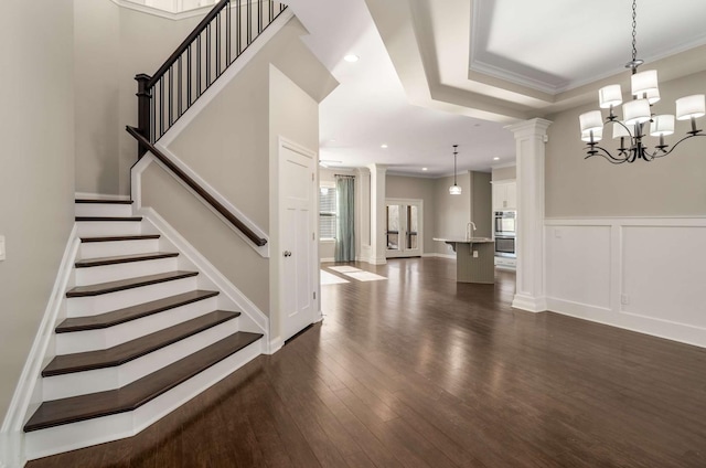 interior space featuring an inviting chandelier, decorative columns, dark wood-style floors, and stairs