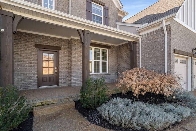 view of exterior entry with a shingled roof, an attached garage, and brick siding