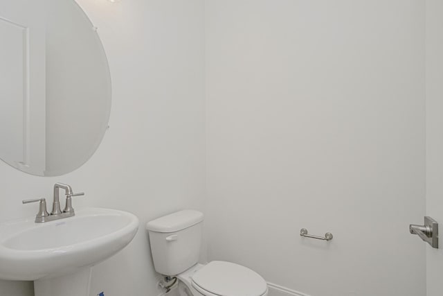 half bath featuring toilet, baseboards, and a sink