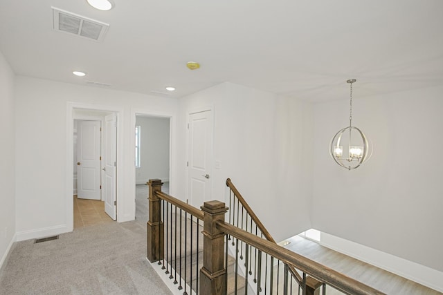 hall featuring visible vents, baseboards, light colored carpet, a notable chandelier, and an upstairs landing