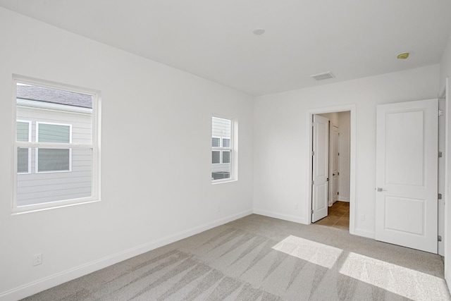 spare room with baseboards, light carpet, and visible vents