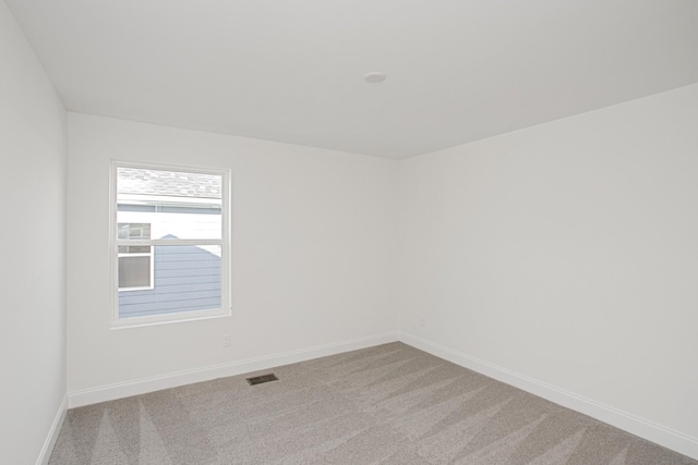 spare room featuring baseboards, light colored carpet, and visible vents