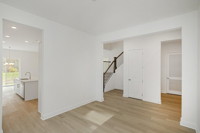 unfurnished room with an inviting chandelier, light wood-type flooring, stairs, and a sink