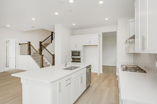 kitchen with appliances with stainless steel finishes, white cabinetry, a sink, recessed lighting, and light wood-style flooring