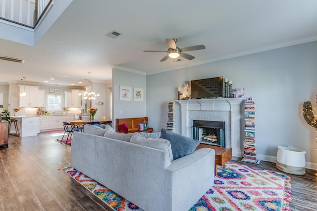 living area featuring crown molding, ceiling fan with notable chandelier, wood finished floors, and visible vents