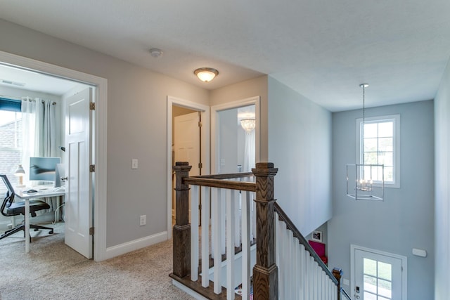 hall featuring an inviting chandelier, carpet floors, visible vents, baseboards, and an upstairs landing