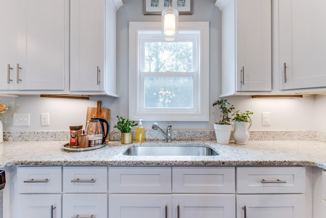 kitchen with white cabinets, light stone countertops, and a sink