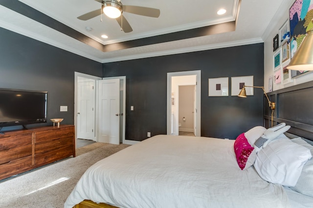 carpeted bedroom with a ceiling fan, ornamental molding, ensuite bathroom, and a tray ceiling
