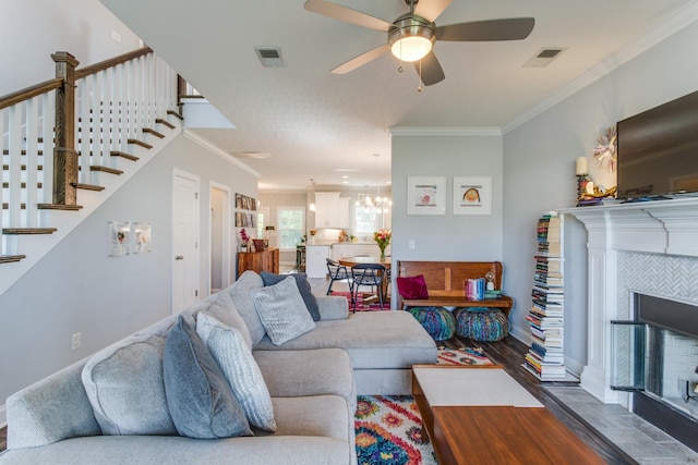 living room featuring crown molding, visible vents, ceiling fan with notable chandelier, and a fireplace