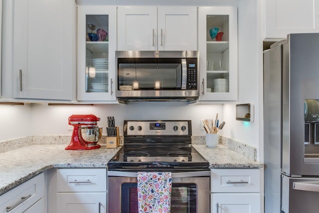 kitchen featuring glass insert cabinets, appliances with stainless steel finishes, white cabinets, and light stone countertops