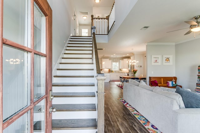 stairs featuring visible vents, ornamental molding, ceiling fan with notable chandelier, and wood finished floors